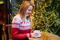 Girl in holiday sweater drinking coffee or hot chocolate in cafe decorated for Christmas Royalty Free Stock Photo