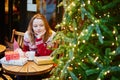 Girl in holiday sweater drinking coffee or hot chocolate in cafe decorated for Christmas Royalty Free Stock Photo