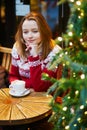 Girl in holiday sweater drinking coffee or hot chocolate in cafe decorated for Christmas Royalty Free Stock Photo