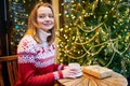 Girl in holiday sweater drinking coffee or hot chocolate in cafe decorated for Christmas Royalty Free Stock Photo