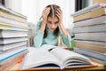 The girl is at home at a desk with high stacks of textbooks holding her head. Royalty Free Stock Photo