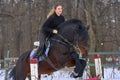 A girl on a horse jumps over the barrier. Training girl jockey riding a horse. A cloudy winter day