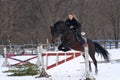 A girl on a horse jumps over the barrier. Training girl jockey riding a horse. A cloudy winter day