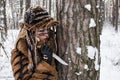 A girl hunter in fur clothes holds a knife stuck in the bark of a tree, because of which she tracks down prey Royalty Free Stock Photo