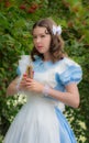Girl in image of fairy tale heroine drinks drink of glass bottle