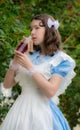 Girl in image of fairy tale heroine drinks drink of glass bottle