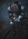 Girl in image of Jeanne d`Arc in armor and with sword in her hands kneels against background of dry grass. Royalty Free Stock Photo