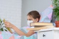 A girl with influenza is reading a book, books are on the nightstand in front of her, focusing on books