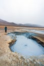 Girl infront of bubbling hot mud pool with mountains and s-shaped road in the background in the Hverarond volcanic area in Iceland Royalty Free Stock Photo