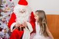 Girl with interest looks like Father Christmas helps to open her gift Royalty Free Stock Photo