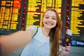 Girl in international airport, taking funny selfie with passport and boarding pass near flight information board Royalty Free Stock Photo