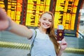 Girl in international airport, taking funny selfie with passport and boarding pass near flight information board Royalty Free Stock Photo