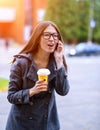 Girl in jacket talking on the phone, emotionally, shouting curses, holding a coffee or tea, young outdoors, sprin