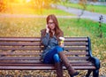 Girl in jacket talking on the phone, sitting a bench, holding coffee or tea, young outdoors, spring fall, life s