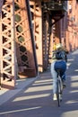 Girl in jeans and backpack riding bike over the bridge