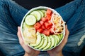 Girl in jeans holding hawaiian watermelon poke bowl with avocado, cucumber, mung bean sprouts and pickled ginger. Top view