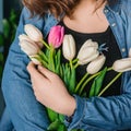Girl in the blue shirt hiding behind flowers tulips in hands on wooden background. A girl in a jeans holds a bouquet of tulips in