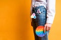 A girl in jeans with a simple dimple keychain holds a rainbow pop it toy in her hand