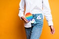 A girl in jeans with a simple dimple keychain holds a rainbow pop it toy in her hand