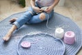 The girl sits on a blue carpet and is engaged in knitting