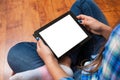 Girl in jeans sits on the floor and holding a black tablet pc with blank white screen. Concept of teenage life and gadgets. Royalty Free Stock Photo