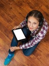 Girl in jeans sits on the wooden floor and holding a black tablet pc with blank white screen. teenage life and gadgets. Royalty Free Stock Photo