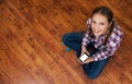 Girl in jeans sits on wooden floor and holding a smartphone. Concept of teenage life and gadgets. Top view with copy space. Royalty Free Stock Photo