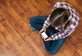 Girl in jeans sits on wooden floor and holding a smartphone. Concept of teenage life and gadgets. Top view with copy space. Royalty Free Stock Photo