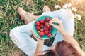 Girl in jeans sitting in summer grass and holding a plate of strawberries
