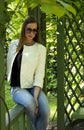 girl in jeans and a white jacket sits in the Park among the greenery, reflected in sunglasses