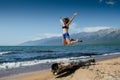 Girl jumping from very old wooden rotten log aground on the beach, near lake Baikal, Russia, on a sunny day in the Royalty Free Stock Photo