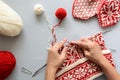 Girl knits red and white jacquard hat knitting needles on gray wooden background. Process of knitting.