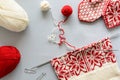 Girl knits red and white Norwegian jacquard hat knitting needles on gray wooden background.