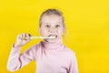 Girl in a knitted sweater holds a toothbrush and smiles at us. Wooden background painted yellow