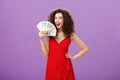 Girl knows how earn money. Successful and delighted satisfied woman in elegant red dress with curly hair holding cash