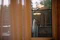 Girl in  lace dress and  long veil looks from  balcony, view through glass , glass of wine is next to,  reflection of chandelier Royalty Free Stock Photo