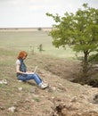 Girl with laptop at rock near lake and tree. Royalty Free Stock Photo