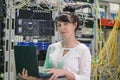 Girl with a laptop is in the server room. Programmer works on the computer in the data center. Woman is on the background of