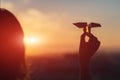 A girl is launching a paper airplane from a window at sunset.