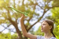 Girl launching toy airplane against green garden and sky, evening lighting.