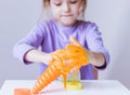 A girl in a lavender long sleeve stretches an orange slime with her hands
