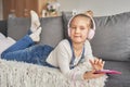 Girl laying on couch in headphones, listening to music with her smarthphone. Little girl watching cartoons on her phone. Listening