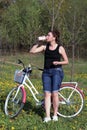 The girl leans on a parked bike. Rest on the spring cycle. The girl drinks water from a bottle Royalty Free Stock Photo