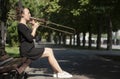 Girl learning to play trombone. Girl plays sitting on a park bench