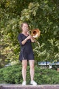 Girl learning to play trombone. Girl plays standing on the alley of a city park