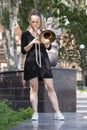 Girl learning to play trombone. Girl plays standing on the alley of a city park