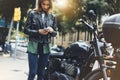 Girl in leather jacket holding smart phone on background motorcycle in sun flare atmospheric city, hipster using in female hands Royalty Free Stock Photo