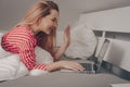 The girl lies on the bed with a laptop. Work from home, laziness. The girl speaks by video link, waves hello Royalty Free Stock Photo