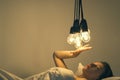 A girl lies in bed under big light bulbs can`t fall asleep. Concept picture. Insomnia. Psychology