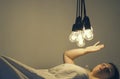 A girl lies in bed under big light bulbs can`t fall asleep. Concept picture. Insomnia. Psychology